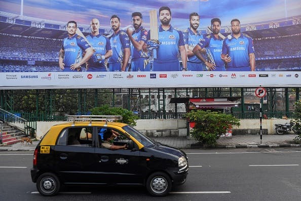 A taxi drives past a hoarding of Mumbai Indians cricketers of the Indian Premier League (IPL) cricket. (Photo by INDRANIL MUKHERJEE/AFP via Getty Images)