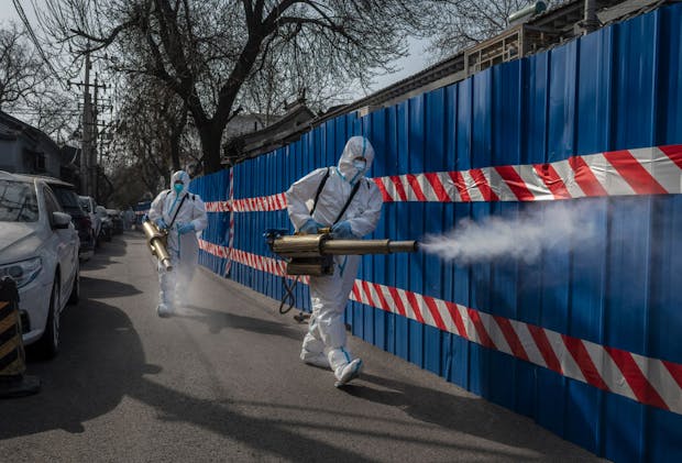 Workers wear protective suits as they disinfect an area outside a barricaded community in Beijing. (Photo by Kevin Frayer/Getty Images)