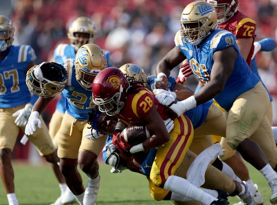 LOS ANGELES, CALIFORNIA - NOVEMBER 20: Keaontay Ingram #28 of the USC Trojans rushes as he is tackled by Mitchell Agude #45 of the UCLA Bruins, losing his helmet, during the first quarter at Los Angeles Memorial Coliseum on November 20, 2021 in Los Angeles, California. (Photo by Harry How/Getty Images)