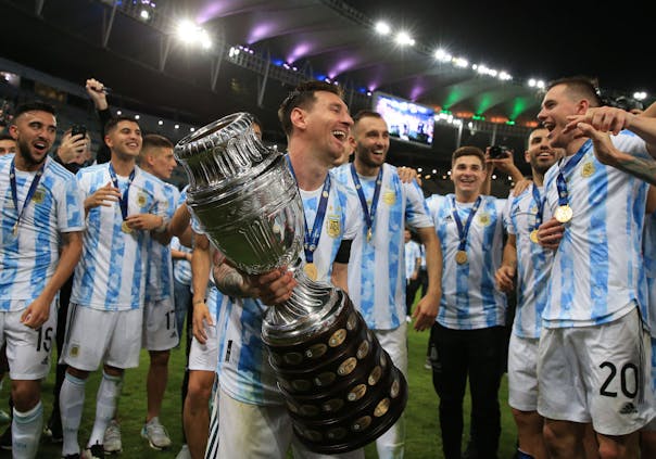 Lionel Messi of Argentina with the trophy as he celebrates with teammates after winning the 2021 Copa America (by Buda Mendes/Getty Images)